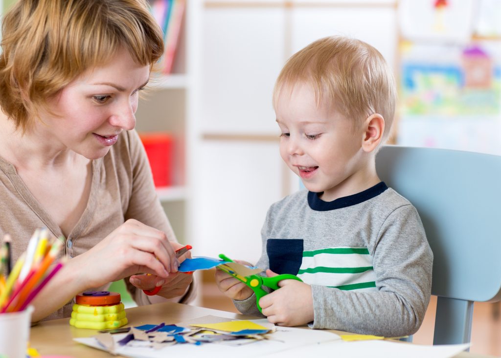 Woman teaches child handcraft at kindergarten or playschool